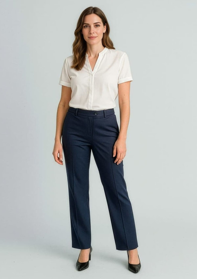 A woman stands in relaxed navy slacks paired with a white shirt. The outfit features a logo on the pants.