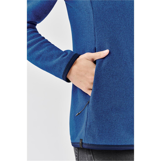 A close-up of a women's blue full zip jacket with a side pocket and contrasting cuffs. It features a logo.