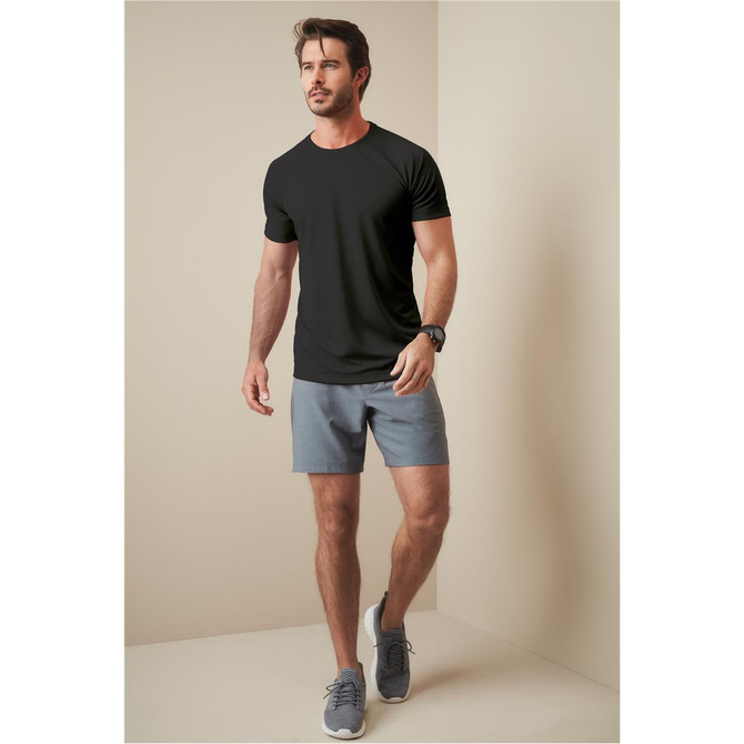 A man wearing a black t-shirt and grey shorts, walking against a neutral background. The t-shirt has a logo.