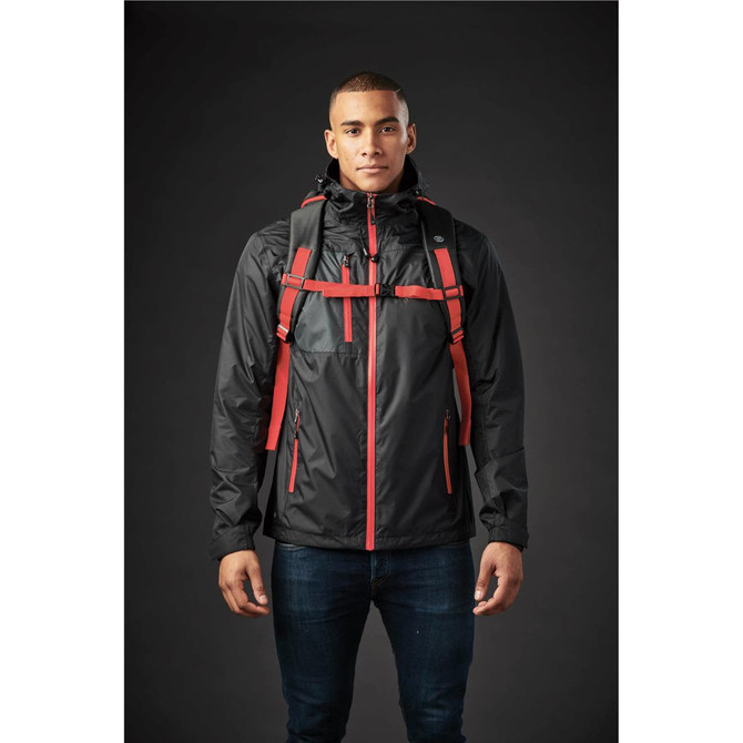 A man wearing a black jacket with red straps and a backpack. The background is dark.