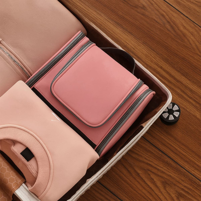 A pink travel large capacity storage bag sits inside a suitcase, accompanied by folded clothing items.