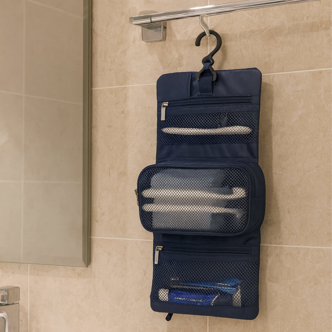 A navy folding travel toiletry bag hangs on a towel rail, featuring mesh pockets and zippers for storage.