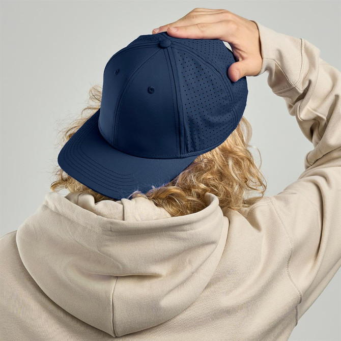 A navy blue cap with ventilation holes, worn backwards on a light-coloured hoodie. The cap features a logo.