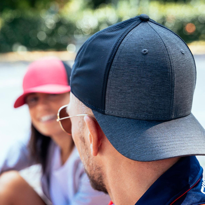 A black cap with a structured design, featuring a logo, worn by a man facing away, with a woman in a pink cap nearby.