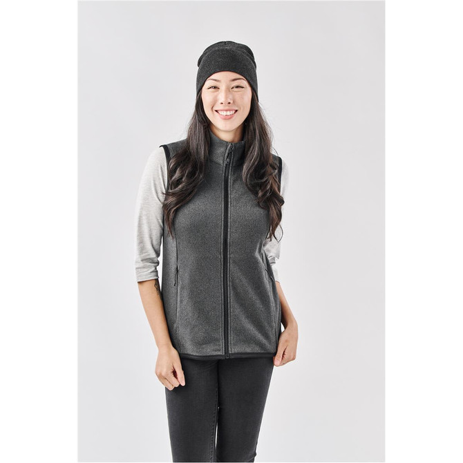 A woman wearing a black Avalante Knit Beanie and a grey vest. The beanie has a branding logo.