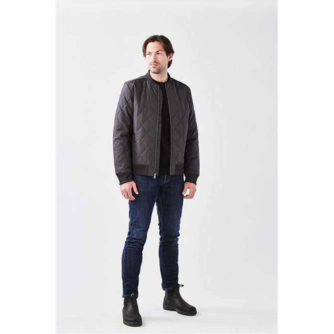 A man wearing a black quilted thermal jacket paired with dark jeans and boots, standing against a neutral background.