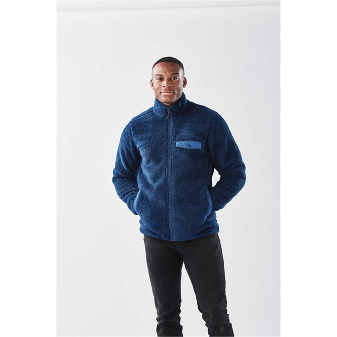 A navy blue men's Bergen Sherpa fleece jacket with a zip front and a pocket. The model is standing with hands in pockets.