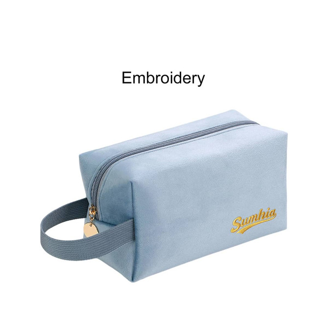 A light blue flannel cosmetic bag with a gold embroidered logo and a handle on one side. 