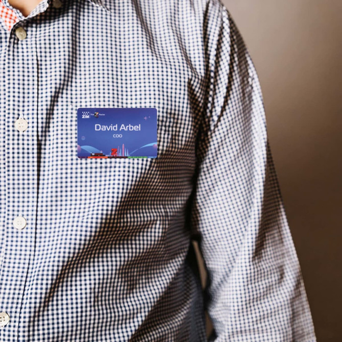 A person wearing a checkered shirt with a blue custom PVC name badge attached. The badge features a logo.