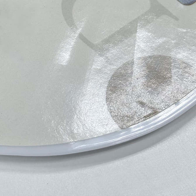 A circular, glossy PVC hand fan featuring a subtle design and clear, flexible edges. It has a light, neutral colour.