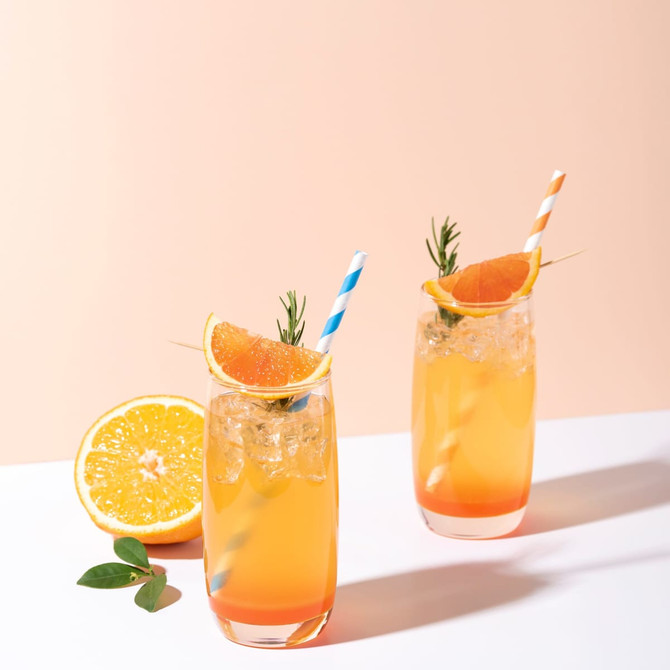 Two tall glasses of orange drinks with ice, garnished with orange slices and rosemary, featuring blue and white striped paper straws.