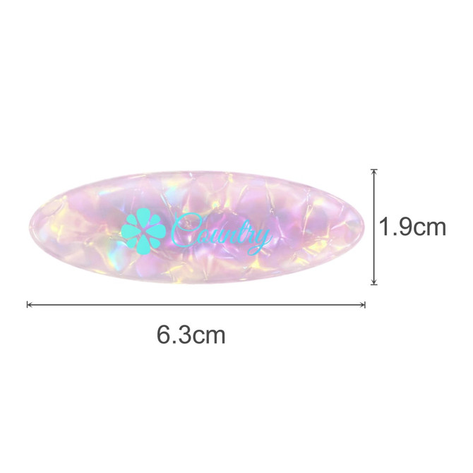 An oval iridescent hair clip in shades of pink and purple, featuring a logo, measuring 6.3cm by 1.9cm.