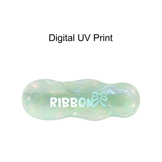 An iridescent alligator hair clip in green and blue tones with a bow design and a logo.