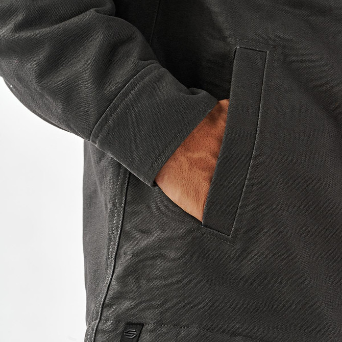 A men's oxford grey canvas jacket with a sherpa lining and side pocket detail. Features a branding tag.