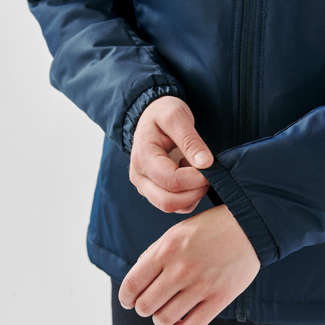 A navy thermal jacket featuring elastic cuffs, with a person's hand adjusting the sleeve. The jacket has a logo.