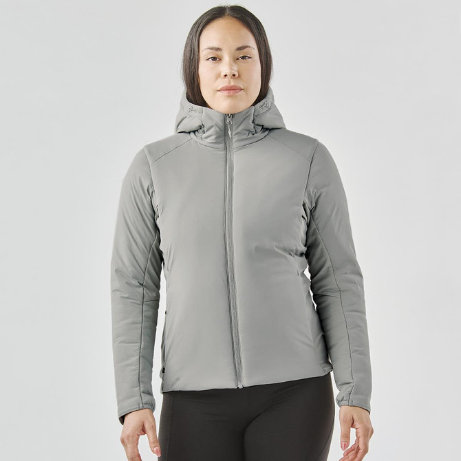 A woman is wearing a grey puffer jacket with a hood. The jacket has a fitted design and features a logo.