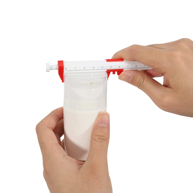 A caliper pen in red and white being used to measure the height of a white bottle, held in two hands.
