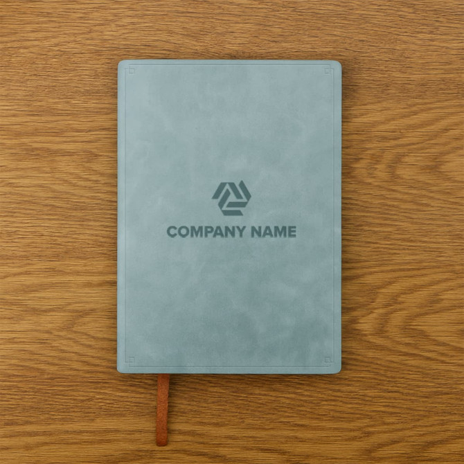 A soft PU leather notebook in a muted green colour with a logo on the cover, placed on a wooden surface.