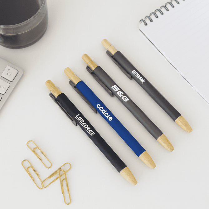 A selection of bamboo click pens in black, blue, and grey, with a notebook and paperclips in the background.