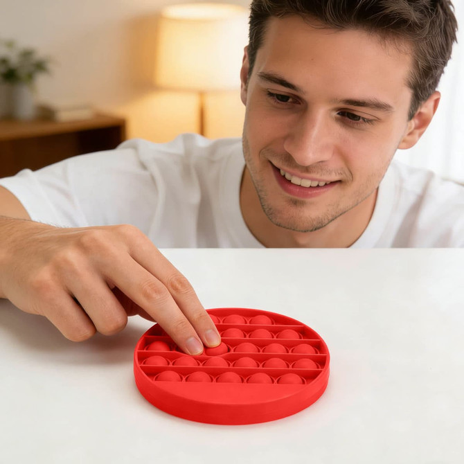 A red fidget toy with multiple poppable bubbles, displayed on a table with a person interacting with it.