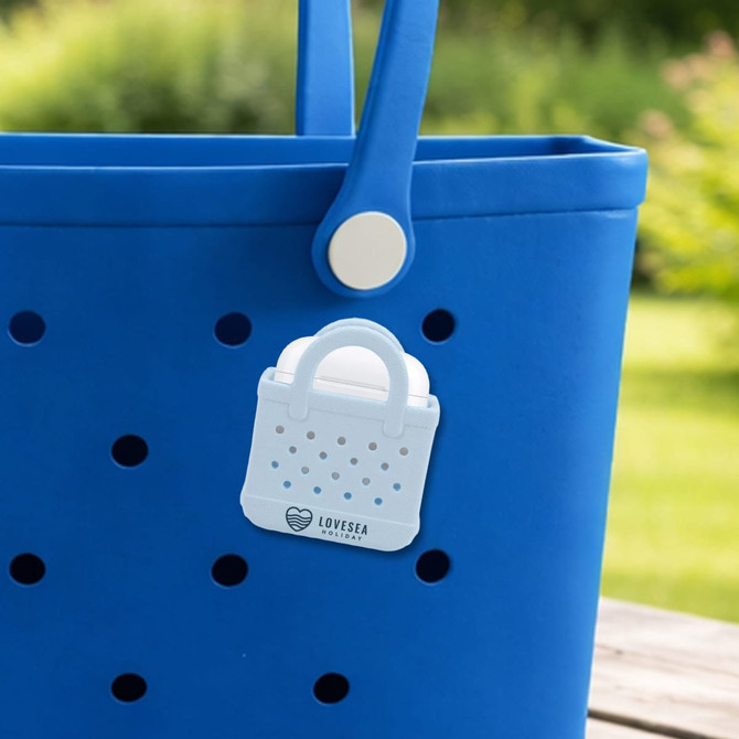A blue tote bag features a white mini EVA holes bag charm attached to it. The charm has a handle and perforated design.