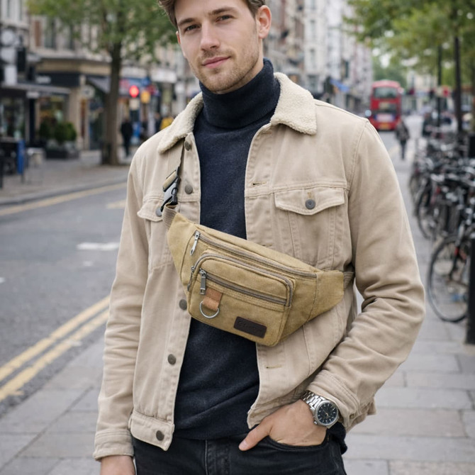 A man wearing a tan canvas waist bag over a black turtleneck, standing on a city street.