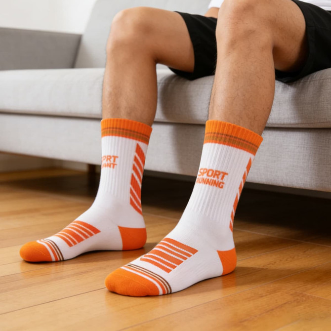 Sport socks with a white base and orange detailing, featuring a logo, displayed on a person's feet while seated.