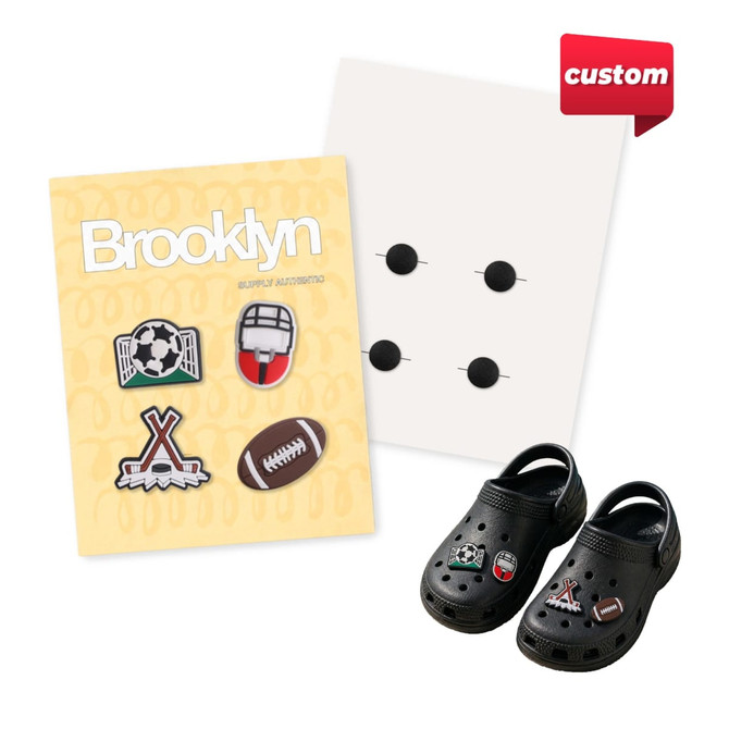 A pack of four custom shoe charms featuring sports designs, displayed alongside a pair of black shoes and a backing card.