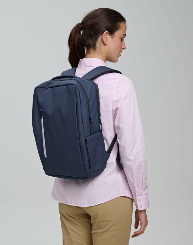 A navy blue backpack with a sleek design is worn by a person facing away, showcasing its minimalist style.