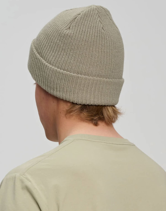 A roll-up cable knit snug beanie in a soft green colour, viewed from the back, featuring a simple logo.