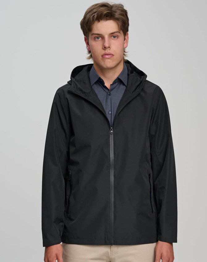 A unisex waterproof jacket in black, featuring a hood and front zipper, modelled by a young man. It has a logo on the sleeve.