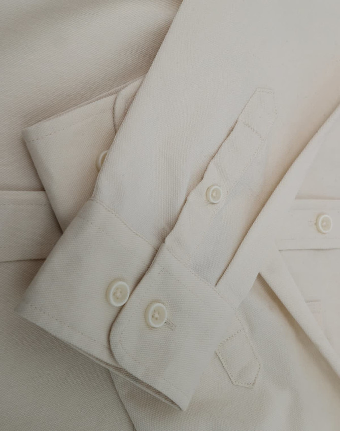 A light beige cotton blend long-sleeve shirt featuring buttoned cuffs and a smooth fabric texture.
