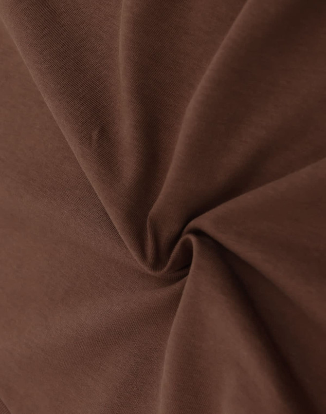 A close-up of brown fabric displaying a smooth, soft texture with a swirling pattern. There is a branding logo visible.