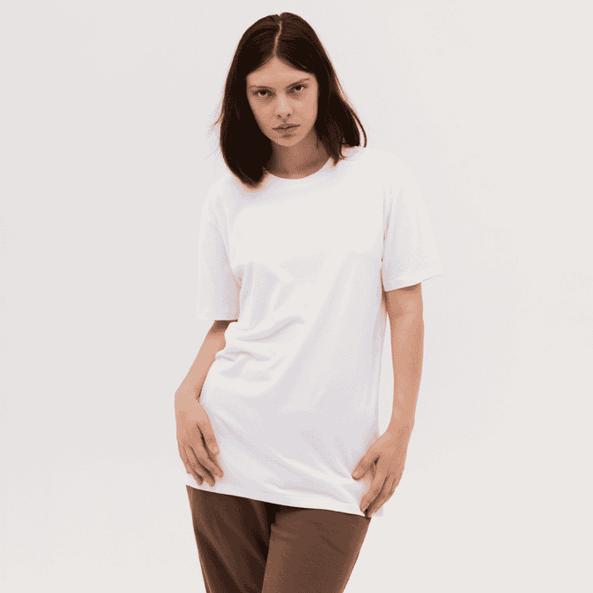A woman wearing a plain white T-shirt, styled with brown trousers, posing against a neutral background.