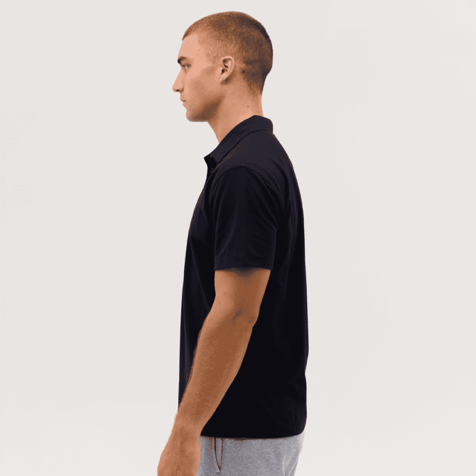 A side view of a black polo shirt on a model, featuring a collar and short sleeves. The shirt has a logo.