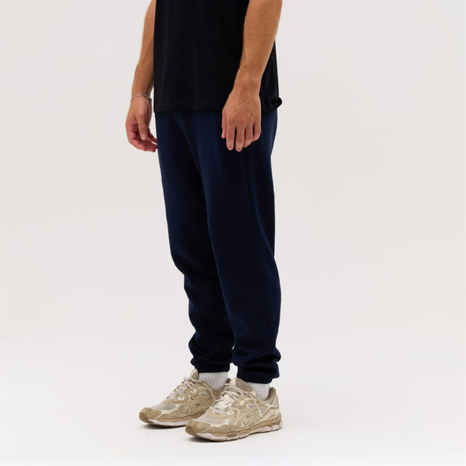 Navy track pants displayed on a person, paired with light-coloured sneakers, set against a neutral background.