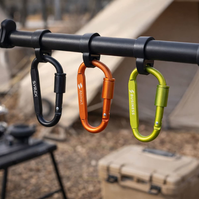 A set of three D shape camping carabiners in black, orange, and green hanging on a pole.