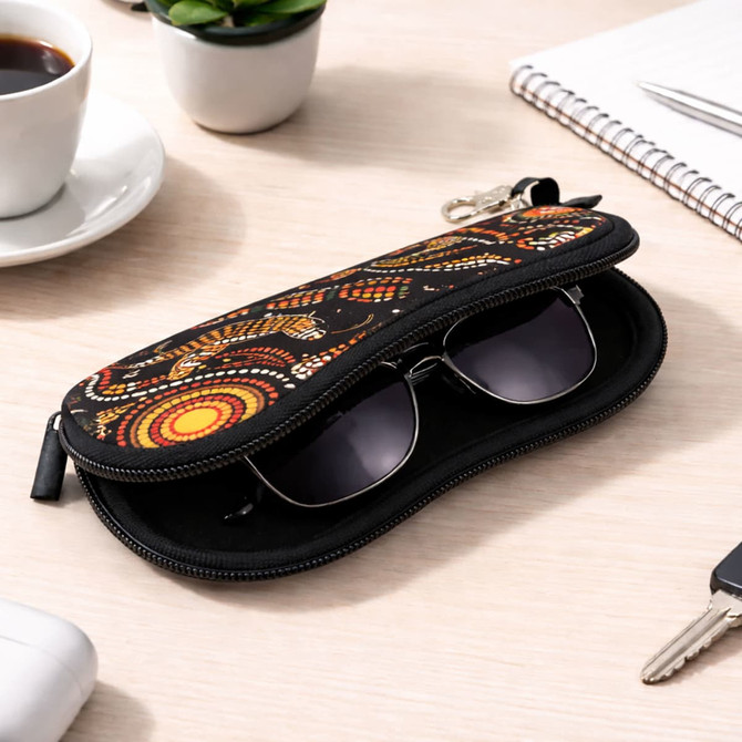 A black neoprene glasses pouch with vibrant indigenous patterns, containing a pair of sunglasses, placed on a desk.