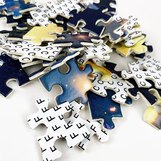 A pile of jigsaw puzzle pieces featuring a cosmic design in blue, yellow, and black hues, with some pieces showing a grid pattern.
