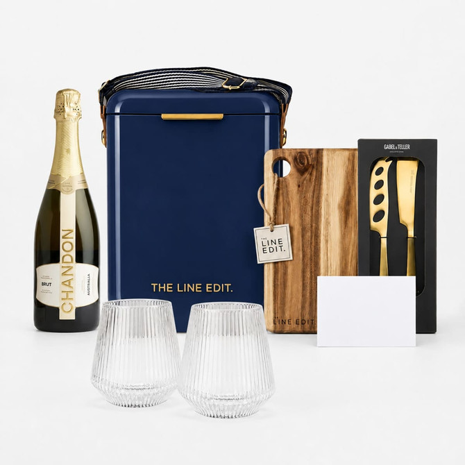 A navy hamper with a drink bottle, two crystal glasses, a wooden board, a corkscrew, and a card. It features branding.