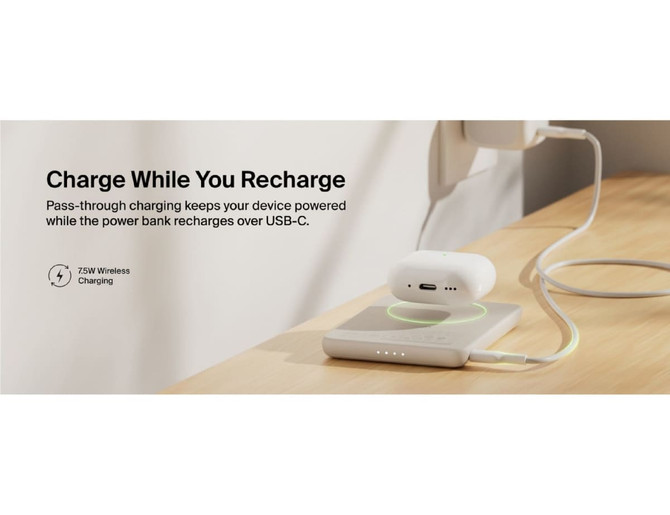 A slim white power bank with a wireless charging pad sits on a wooden surface, connected by a USB-C cable.