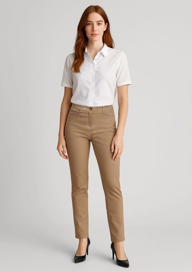 A woman stands wearing slim leg stretch chino pants in tan and a white collared shirt, paired with heels.