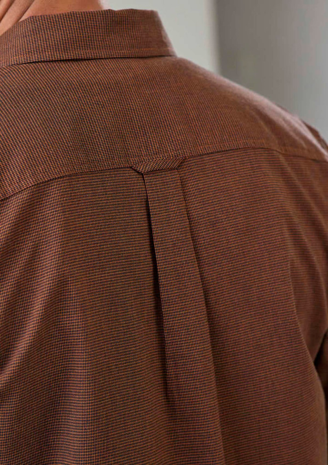 A brown patterned long sleeve shirt featuring a back pleat and a collar, with a logo on the garment.