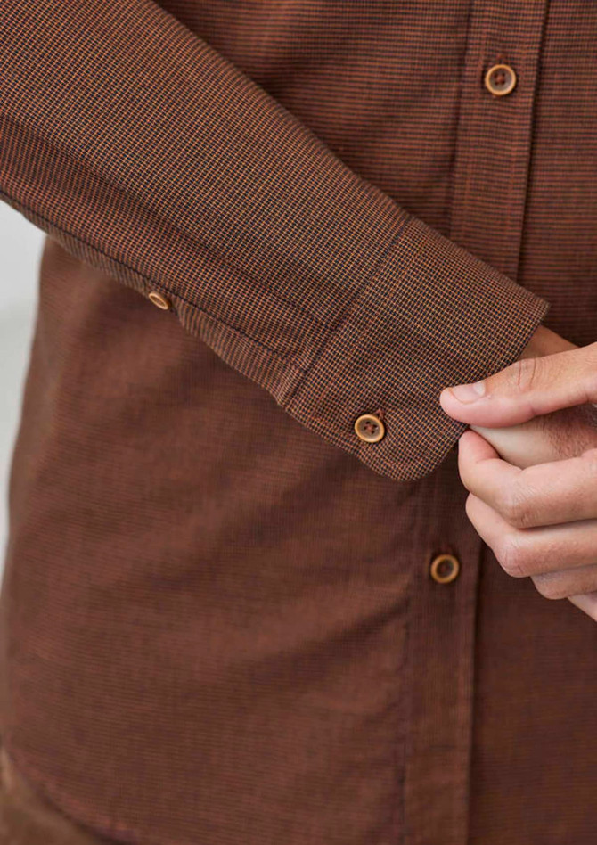 A button-up shirt in a warm brown tone, featuring a check pattern and buttoned cuffs. It has a logo branding.