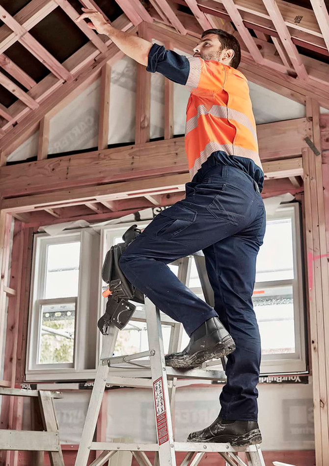 Men's cargo pant in navy, worn by a man on a ladder, working in a partially constructed building. The pants have pockets and a logo.