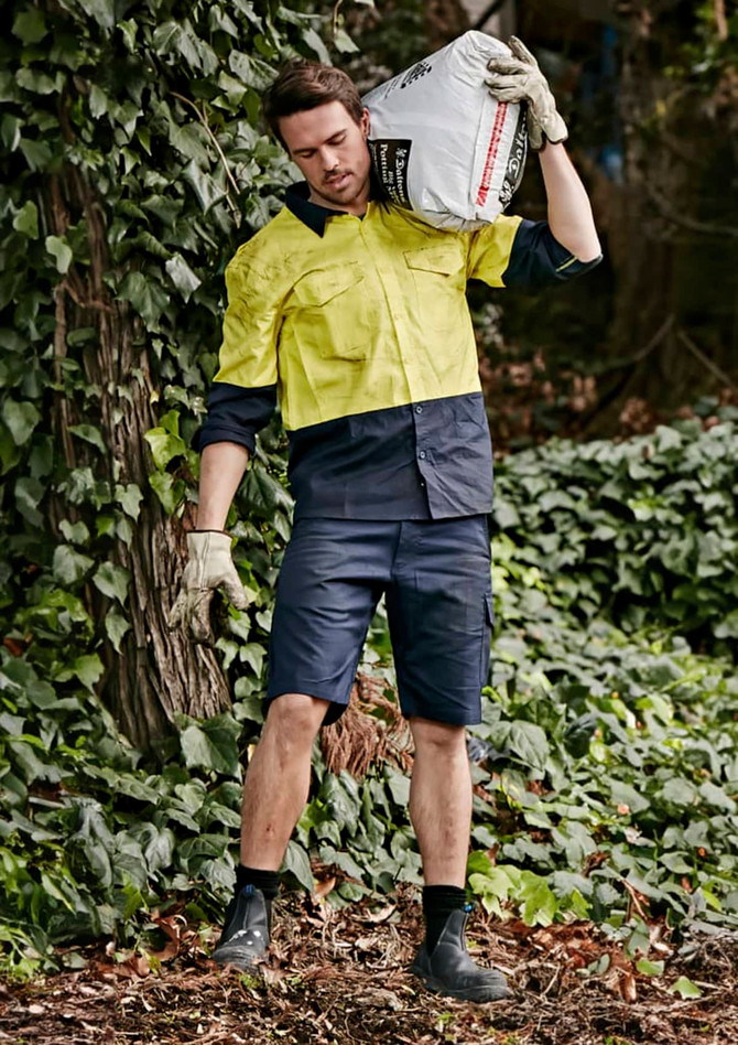 Men's rugged cooling vented shorts in navy, styled with a bright yellow shirt, set against a leafy background.