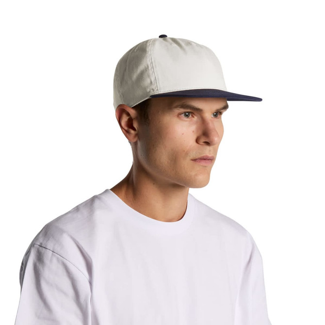 A two-tone cap featuring a white crown and a navy peak, with a person wearing it. The cap has a logo.