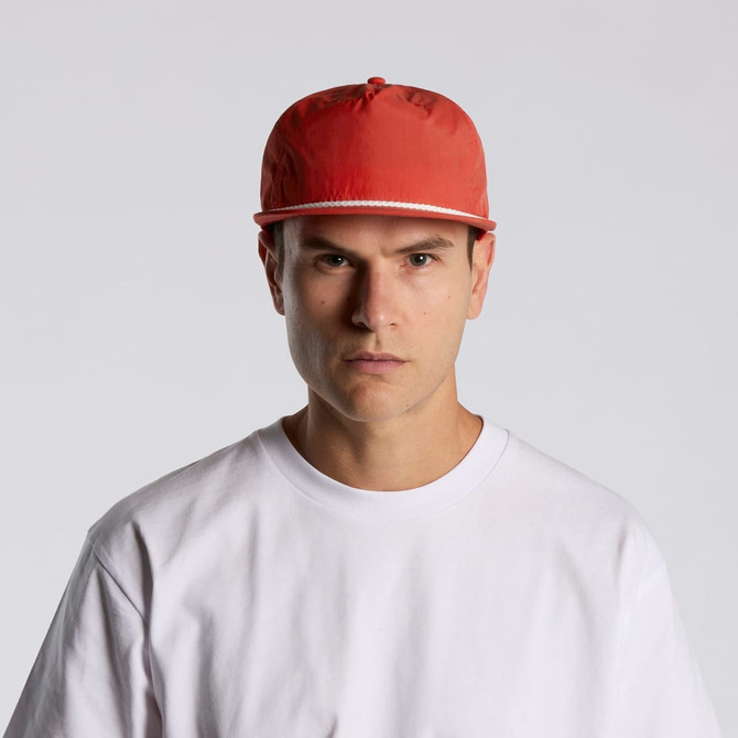 A red cap with a flat brim is worn by a model in a plain white T-shirt. The cap features a logo on the front.