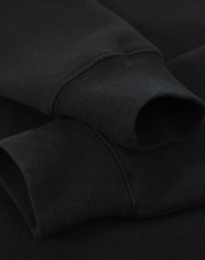 A black crew fleece jumper featuring ribbed cuffs, showcasing a soft fabric texture. It has a branding logo.