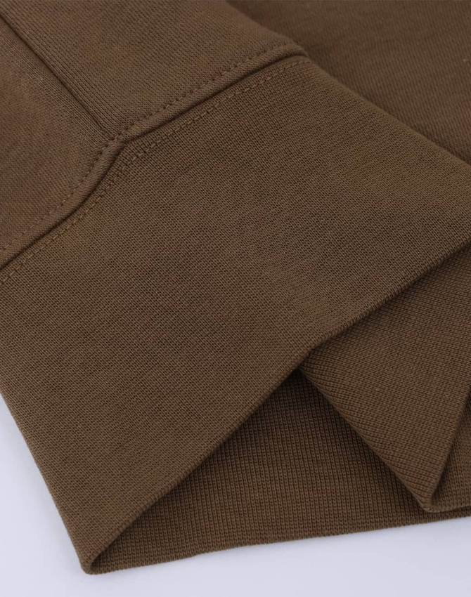 A close-up of a folded brown crew neck sweatshirt featuring ribbed cuffs and a subtle texture. Designed with a logo.
